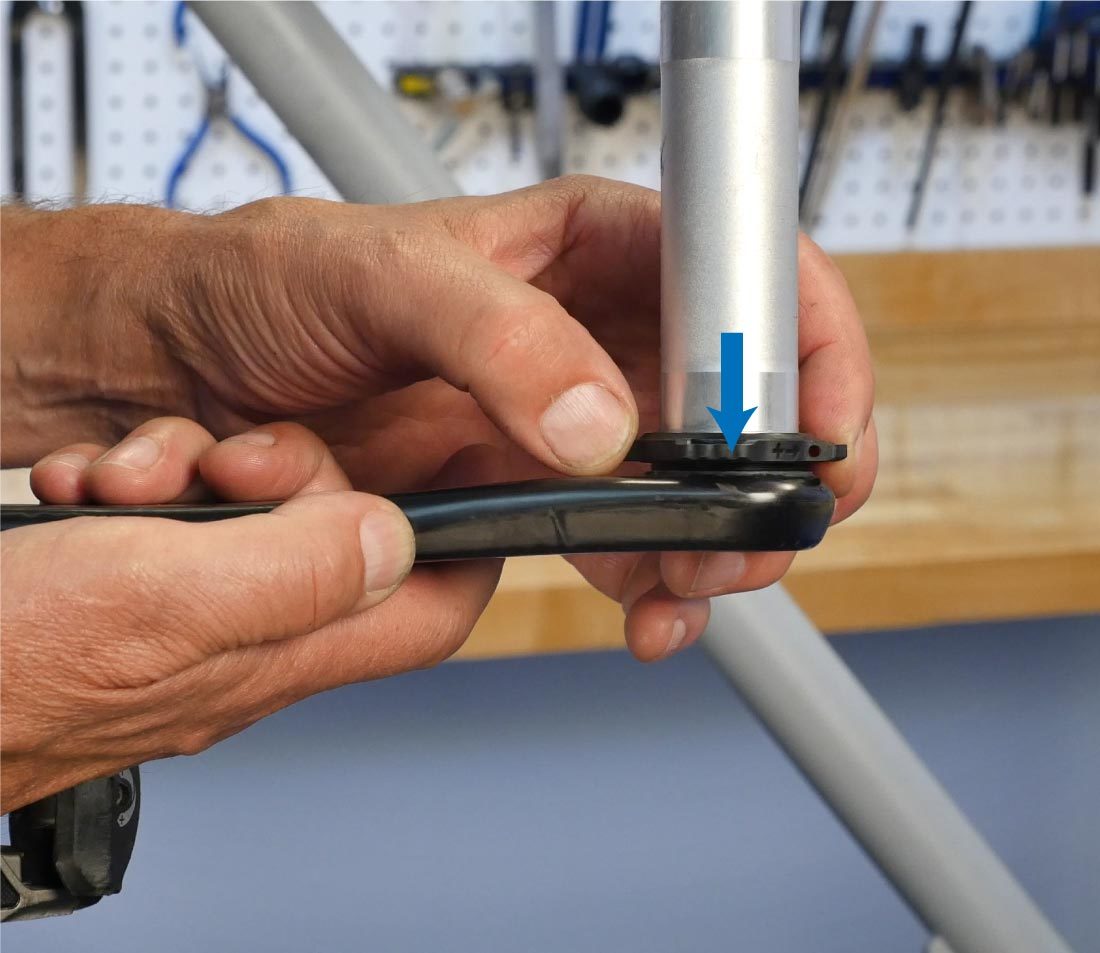 Holding non-drive side crank arm vertically with arrow indicating hand pressing ring down the spindle