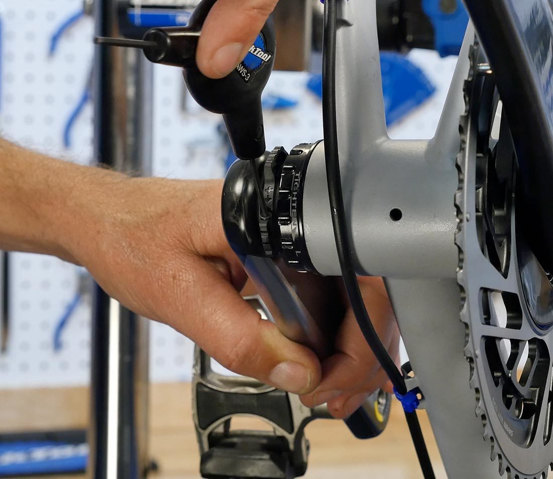 Hand holding non-drive side crank arm while hand tightening preload ring pinch bolt using AWS-3 hex wrench