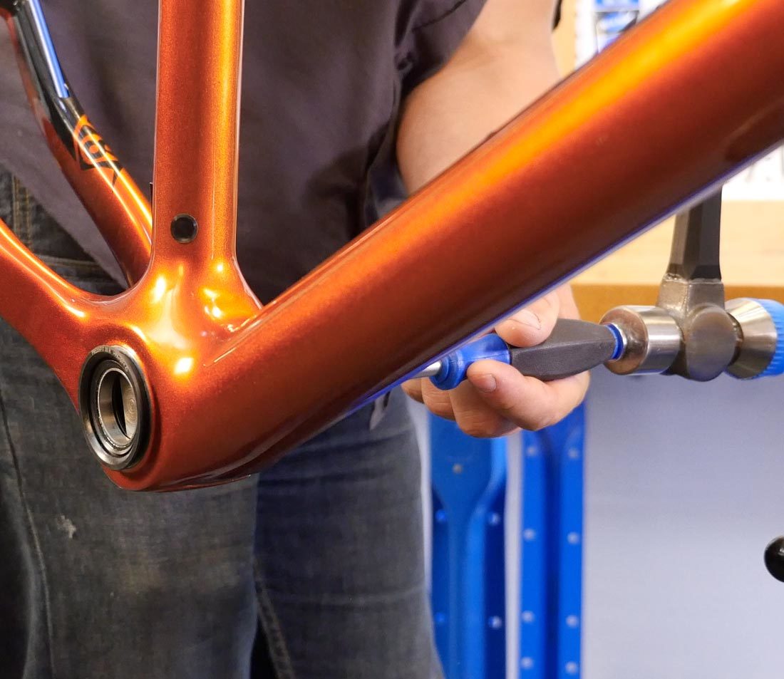 Hammer hitting handle of BBT-30.4 to drive press fit bearing cup out of bottom bracket shell on orange bike