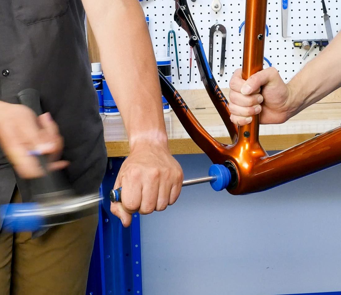 Hammer hitting handle of BBT-30.4 to drive press fit bearing cup out of bottom bracket shell on orange bike