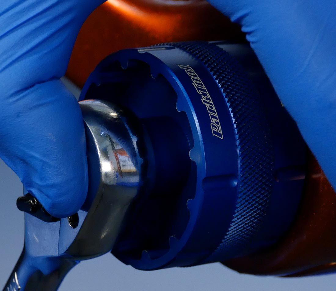 Thumb pressing against socket wrench while bottom bracket tool loosens thread-together bottom bracket