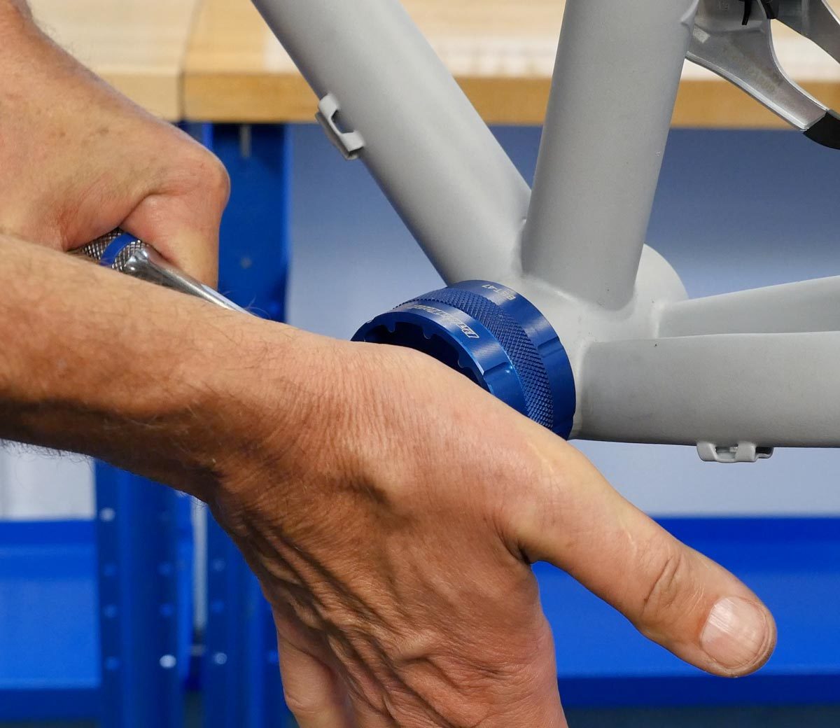 Palm of hand applying pressure to back of socket wrench with bottom bracket cup tool fitted to cup