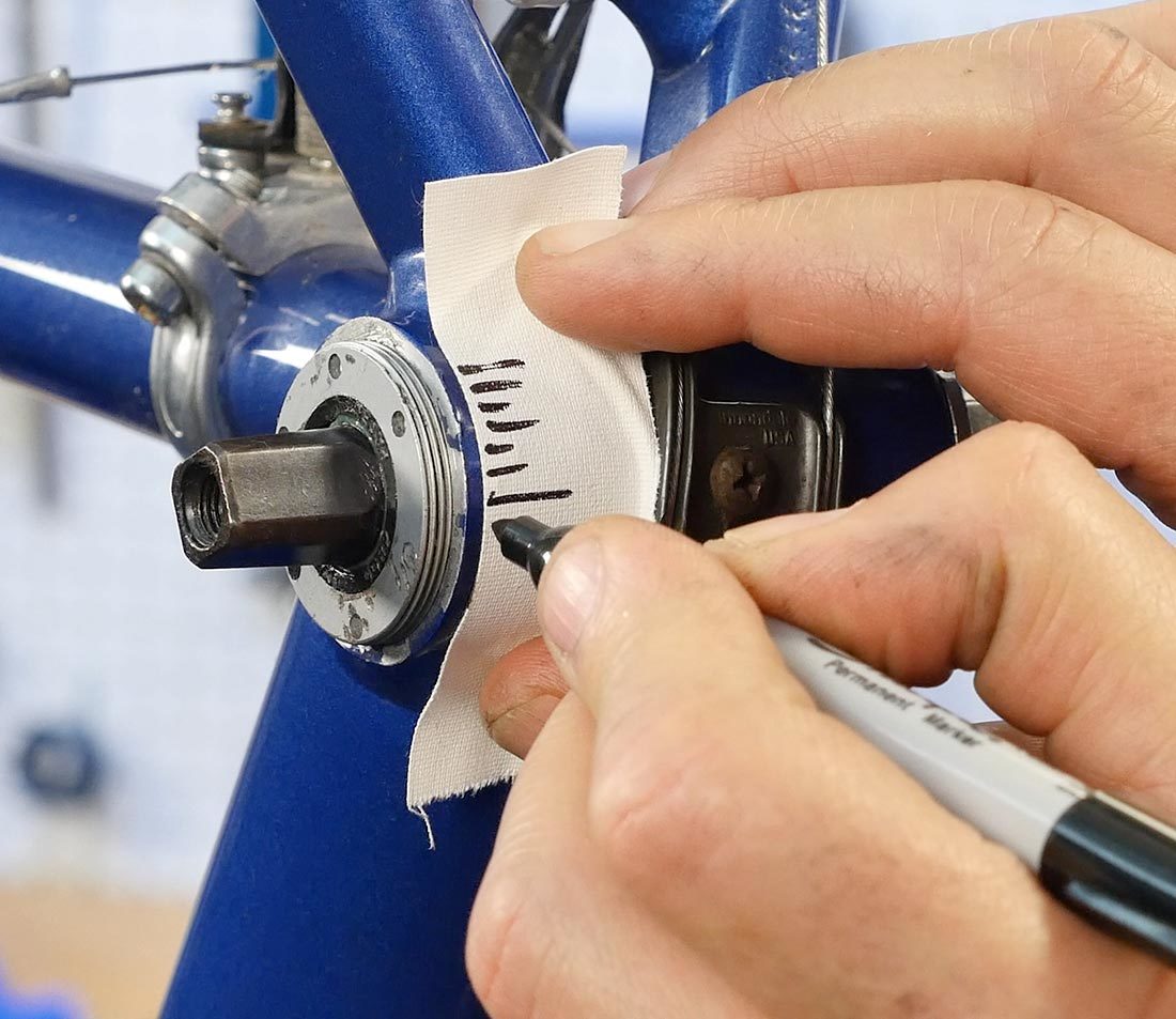 Permanent marker making reference lines on white tape applied to underside of bottom bracket shell
