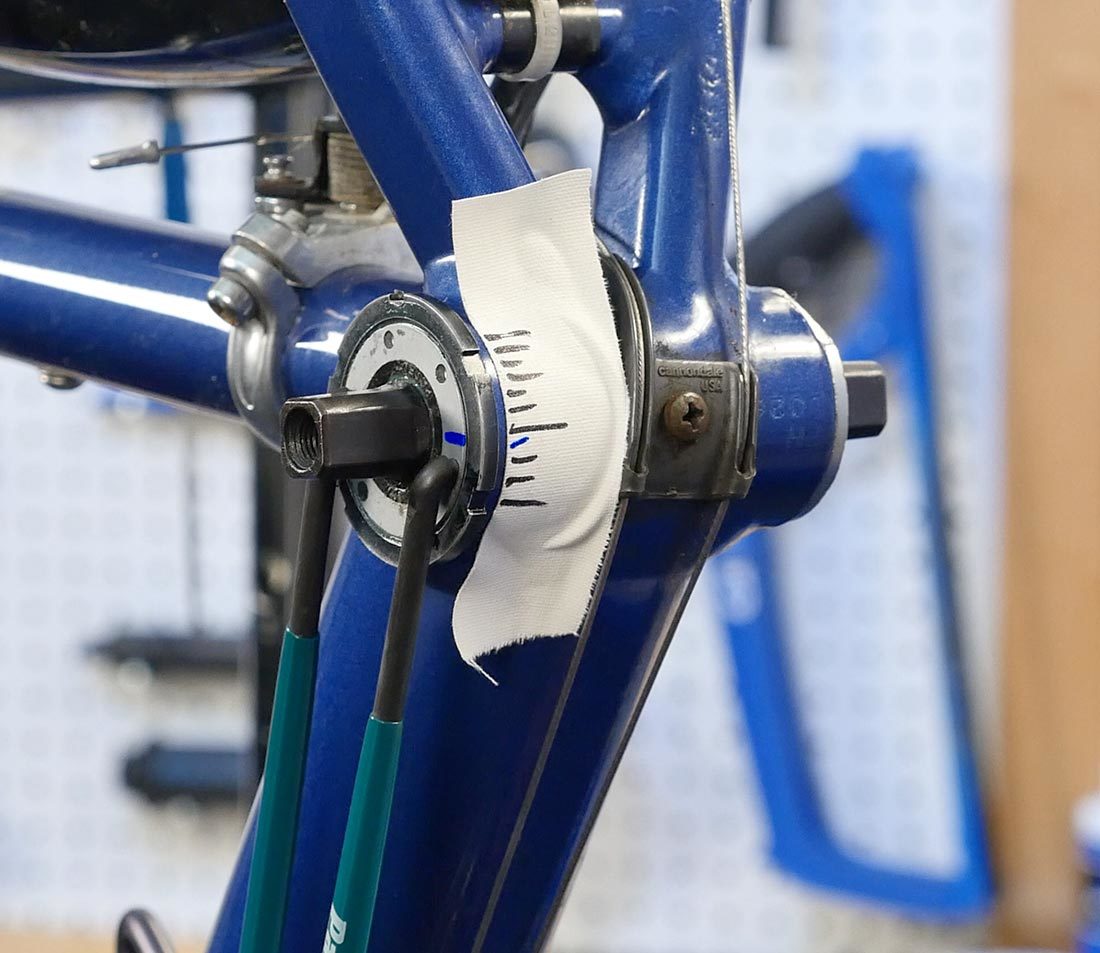 Pin spanner adjusting bottom bracket cup with blue marks on tape and cup for reference