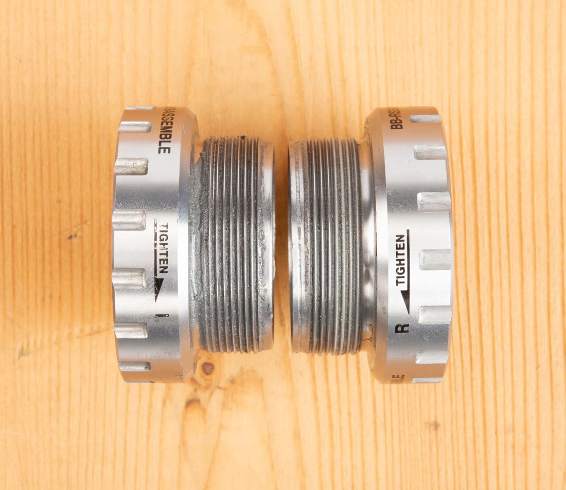 Closeup of two sides of external bottom bracket cups on a workbench, with arrows indicating threading
