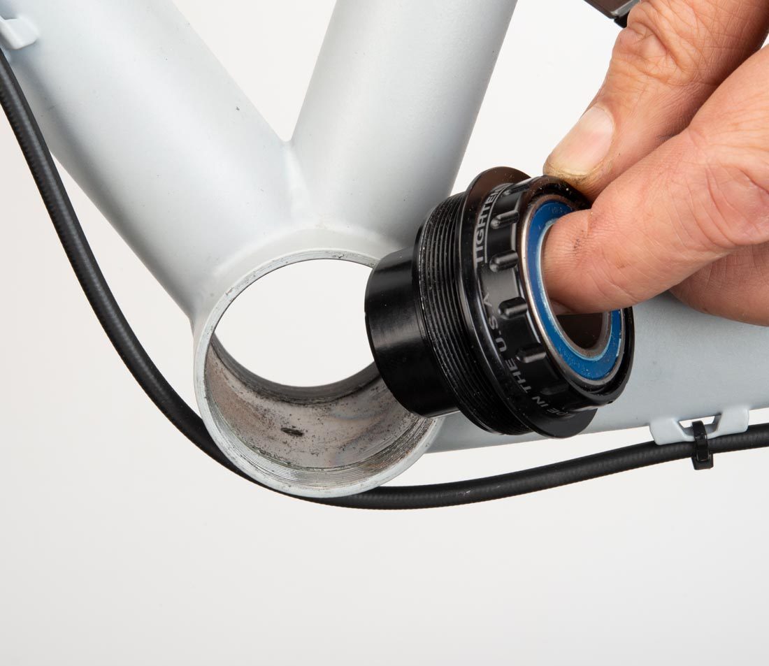T47 bottom bracket cup held next to T47 threaded bottom bracket shell on gray alloy bicycle frame