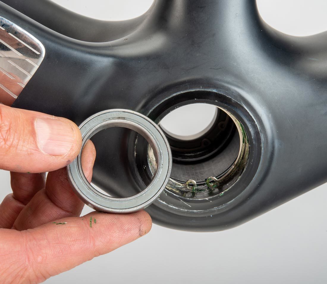 PF42 bottom bracket bearing held next to compatible bottom bracket shell of carbon fiber bicycle frame