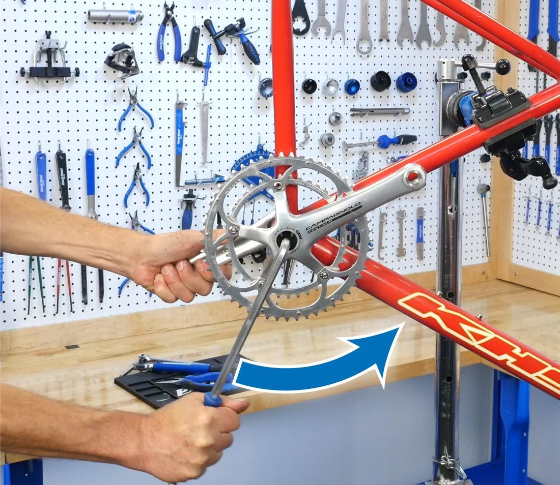 Hex wrench turning crank bolt counterclockwise with hand holding non-drive side crank of bike in repair stand
