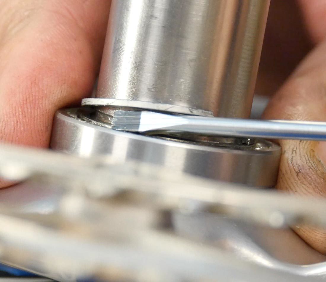 Closeup of small flat blade screwdriver prying up C-clip from base of drive side crank spindle