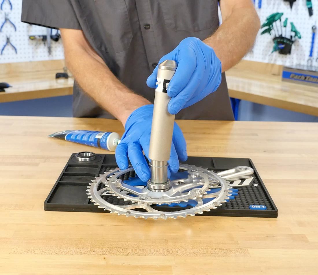 Hand pressing bearing driver onto C-clip to push it down a drive-side crank spindle