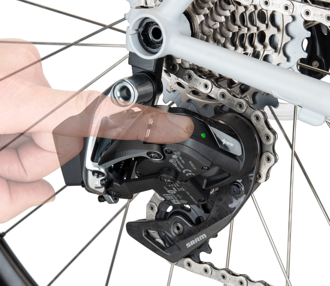 Finger pressing button on rear AXS® derailleur mounted on a bicycle with green light illuminated
