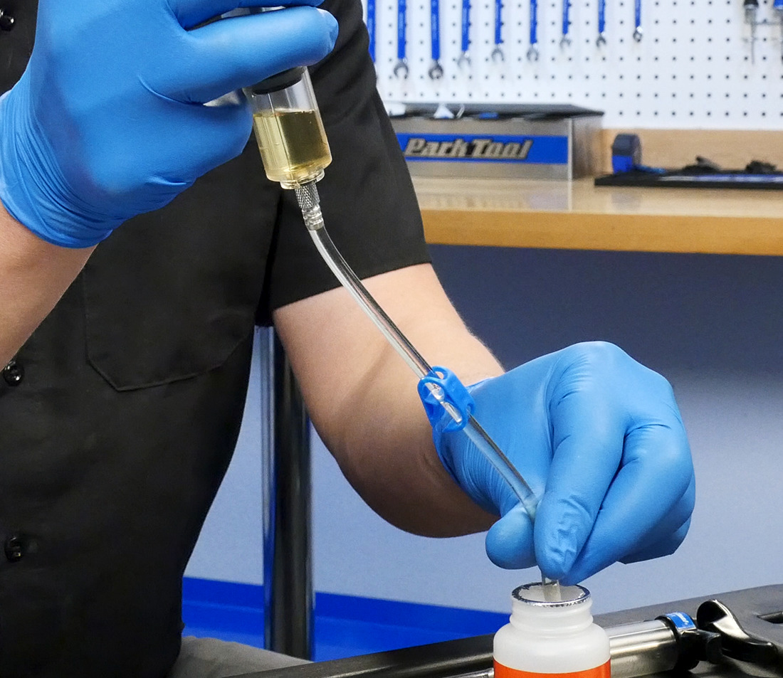 Brake bleeding syringe using hose to draw hydraulic brake fluid out of a container