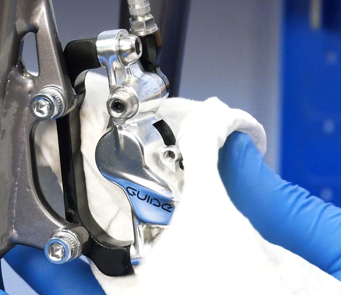 Hydraulic disc brake caliper on rigid bicycle fork being wiped with a clean rag