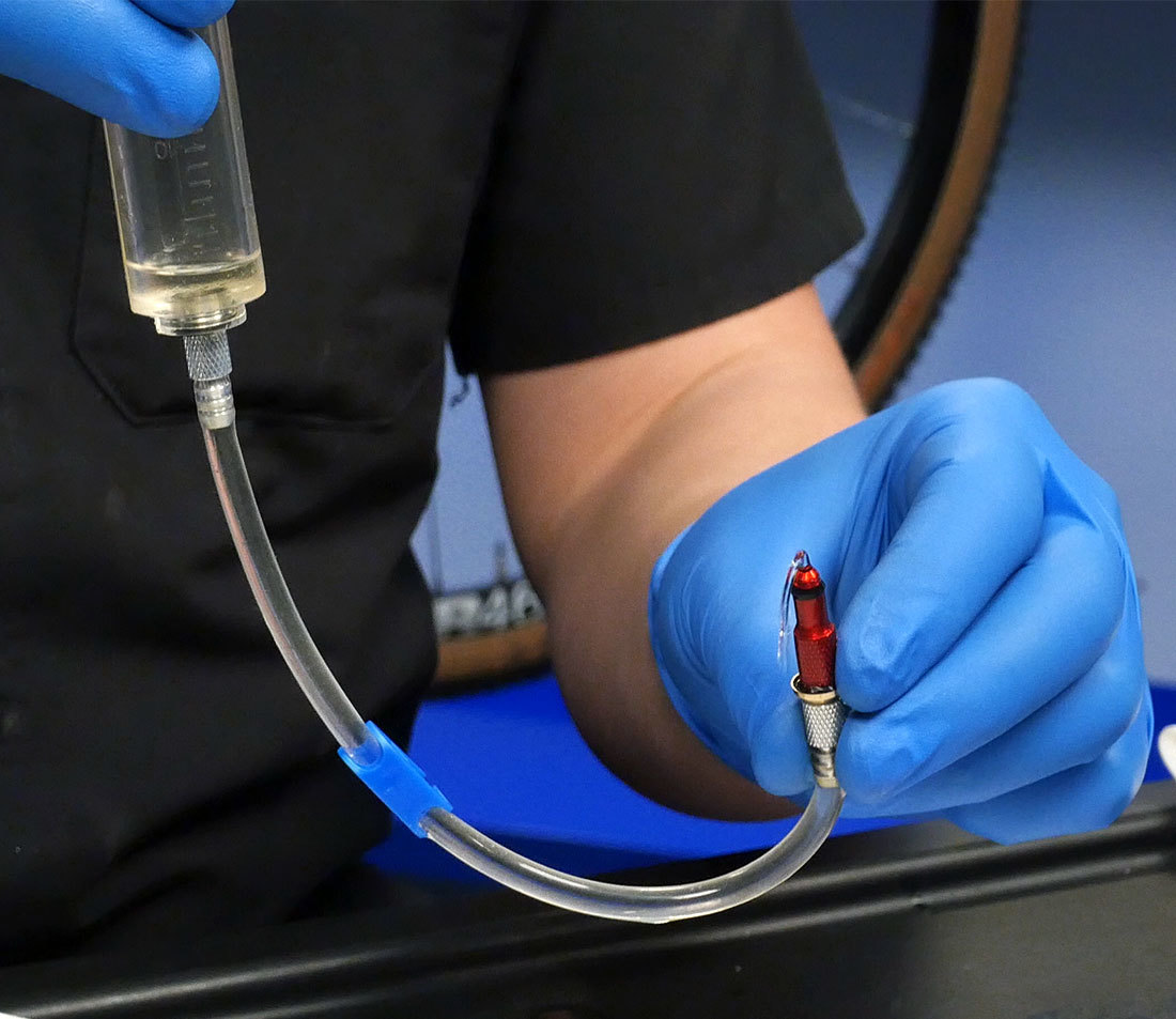 A bleed syringe held in one hand and hose end in the other, working alcohol back and forth