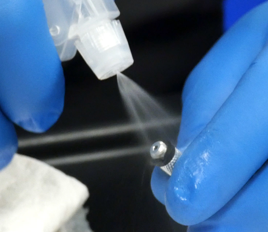 Threaded hose end being sprayed with rubbing alcohol