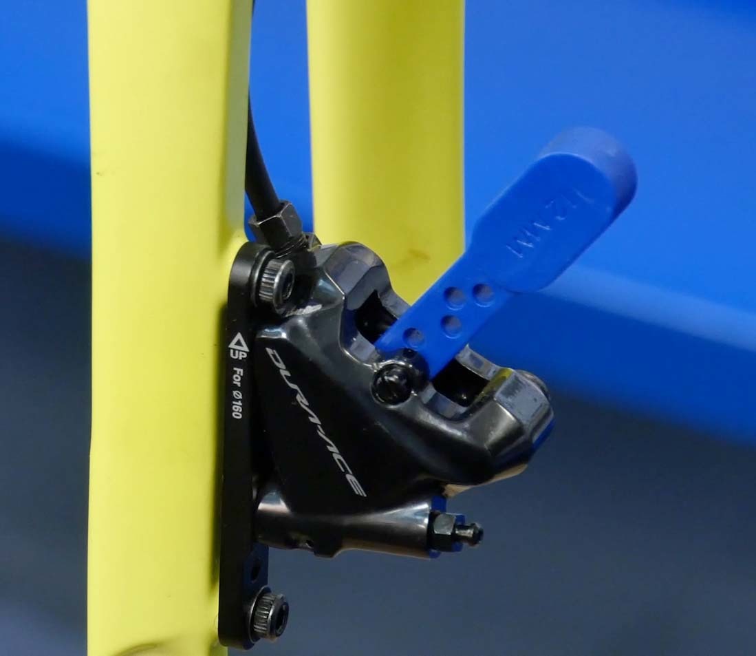 Bleed blocks inserted into hydraulic caliper mounted to a yellow rigid bicycle fork