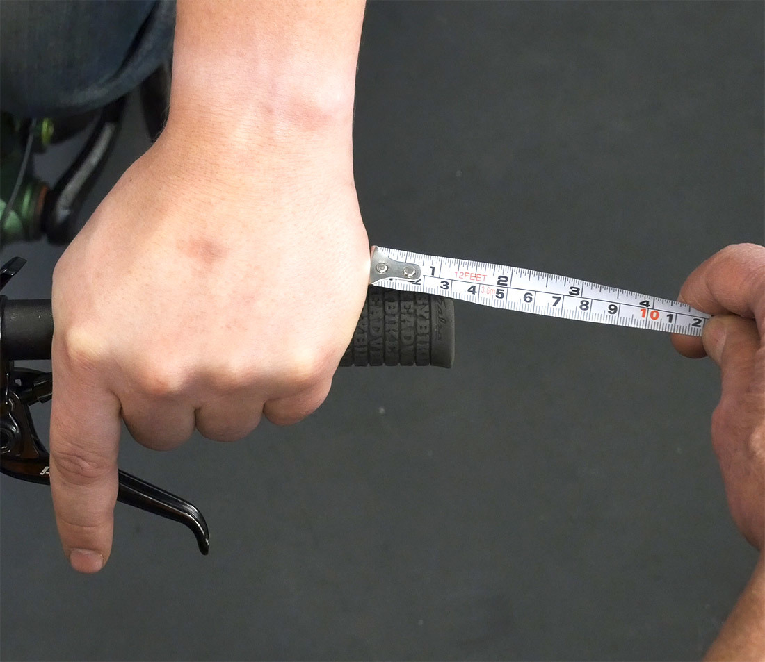 A tape measure measuring the distance from the outside of a person's hand to the outside of the handlebar grip