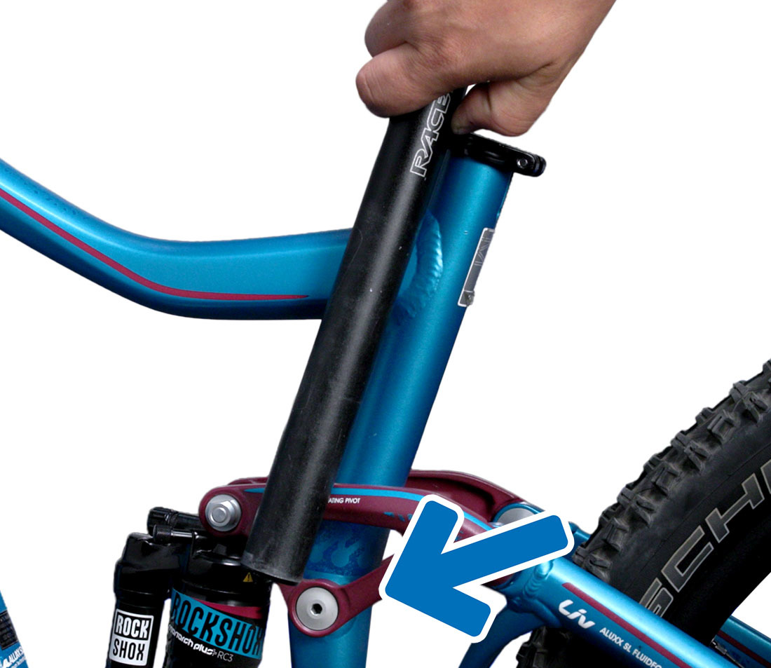 Detail shot of a seat post next to a bicycle frame, with an arrow pointed to the frame's suspension linkage.