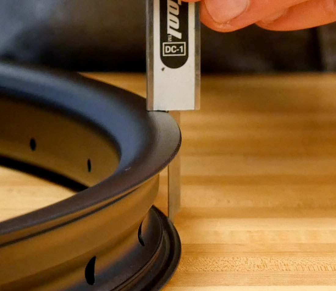 Resting digital caliper end on rim face with rod extended to measure rim diameter