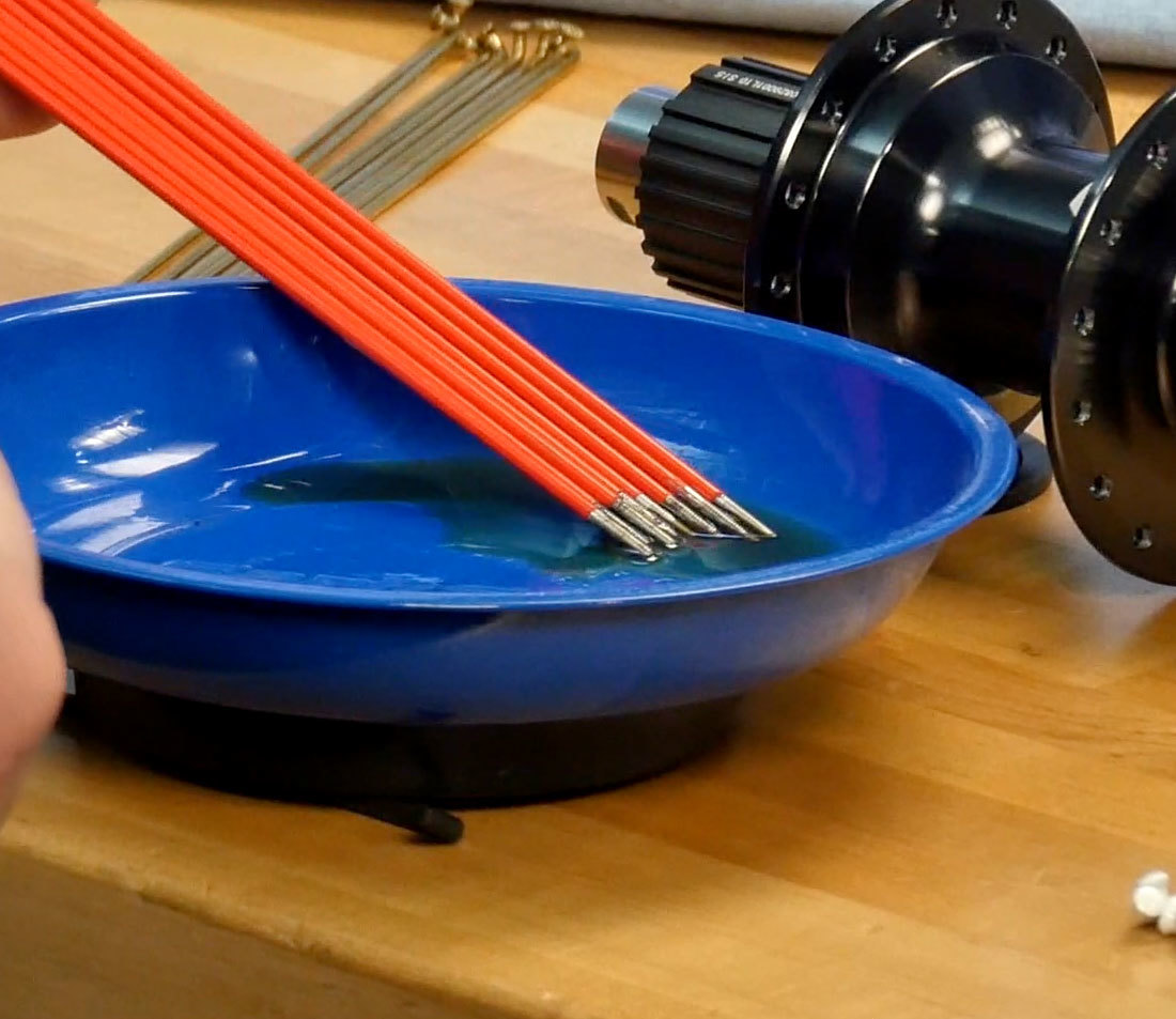 Threaded spoke ends resting in magnetic bowl with lubricant